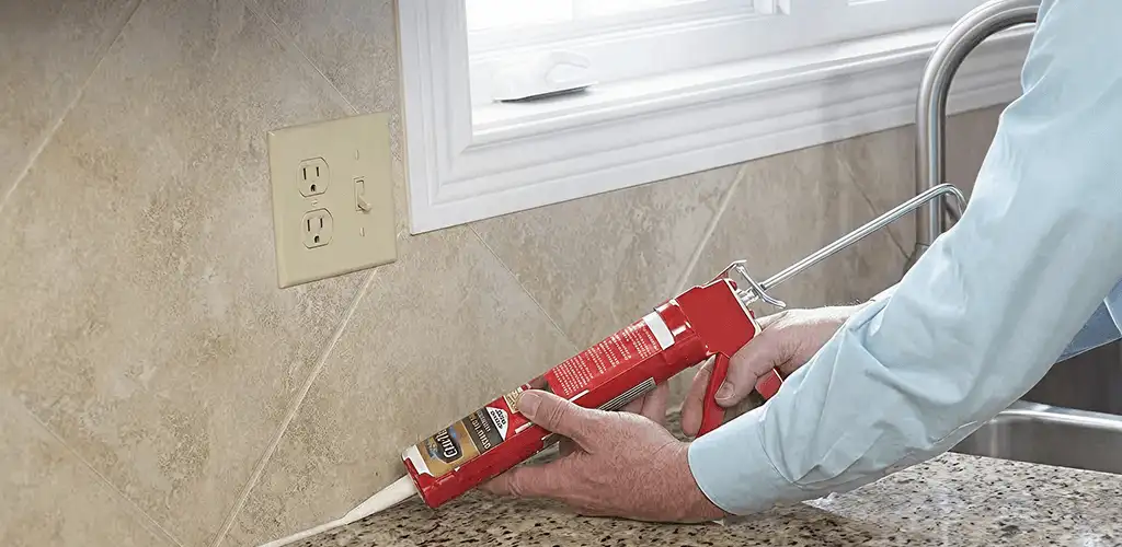 Handyman applying caulk along a kitchen backsplash and countertop seam in Erie, PA