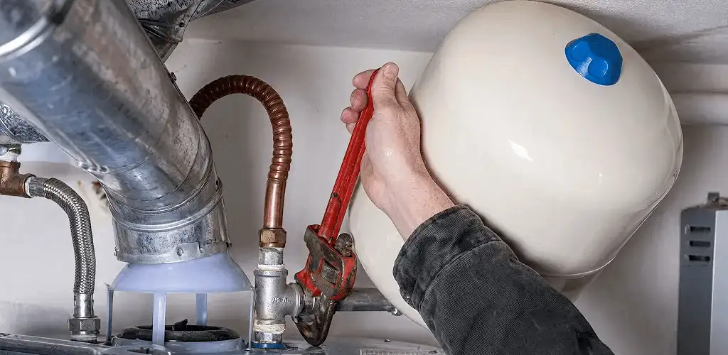 Water heater repair technician tightening plumbing connections near a tank unit in Erie, PA